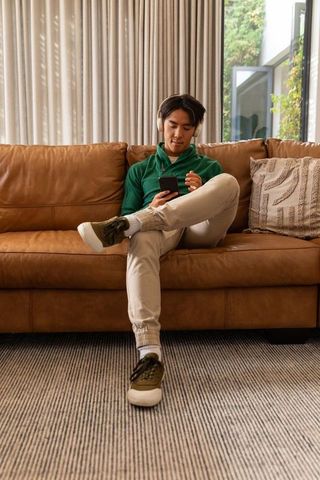 Young asian man relaxing on leather sofa listening to music with headphones and smartphone
