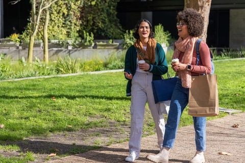 Friends walking and chatting with coffee and shopping bags in sunlit urban park