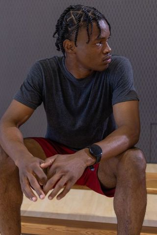 African-american athlete sitting on bench checking smartwatch after intense gym workout