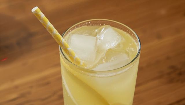 Chilled lemonade with ice cubes, lemon slice and patterned yellow straw on wooden tabletop