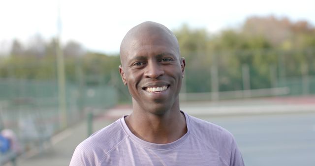 Portrait of happy african american male tennis player on sunny court. Sport, fitness, health and outdoor activities, unaltered.