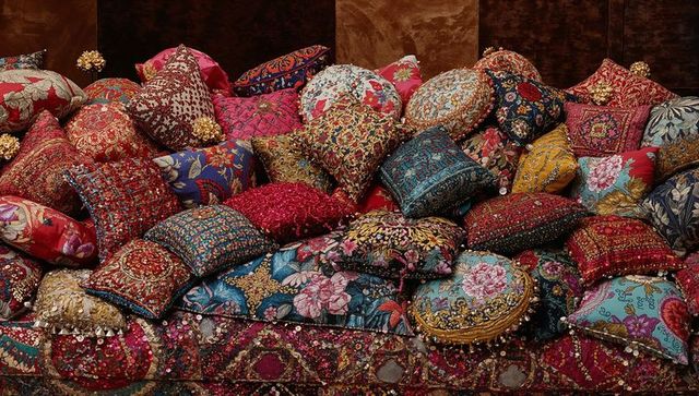 Piled embroidered cushions on patterned velvet sofa showcasing ornate tassels and beads
