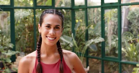 Smiling Woman in Yoga Attire with Braided Hair in Greenhouse