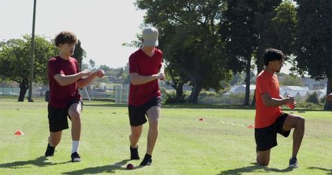 Young men practicing knee drills on grass with cones and red training ball for conditioning