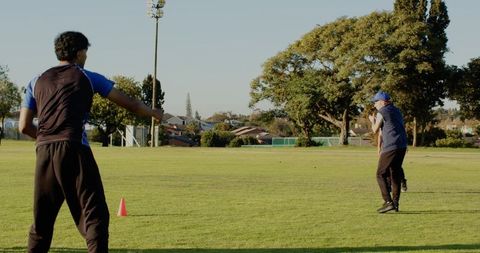 Coach pointing during outdoor team practice on grass field, players preparing cone drill