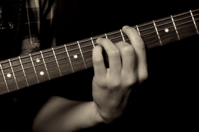 Hand playing guitar close-up in sepia tone. Suitable for music-related projects, guitar tutorials, practice guides, promotion of music lessons, band promotions or creative compositions. Highlights skill and focus of musician.