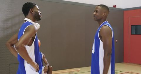 Basketball teammates discussing strategy on indoor court wearing blue white jerseys