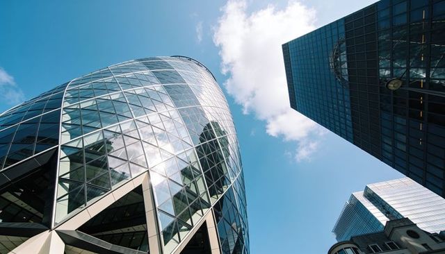 Curved glass tower with diamond grid glazing reflecting blue sky and city skyscrapers