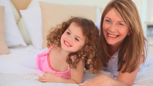 A grandmother and her granddaughter share a joyful moment on the bed, embodying warmth and familial connection. This can be used for parenting blogs, family publications, or websites promoting family bonding and happiness.