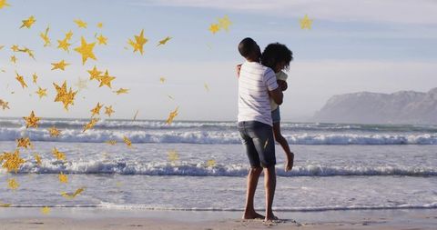 African american father carrying daughter on beach with golden star confetti overlay
