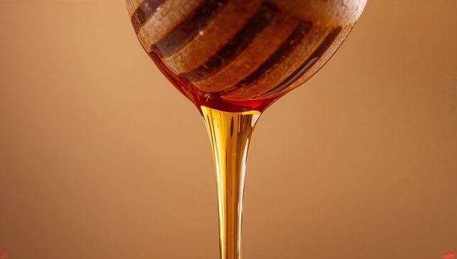 Amber Honey Pouring from Grooved Wooden Dipper Closeup Dripping Viscous Stream