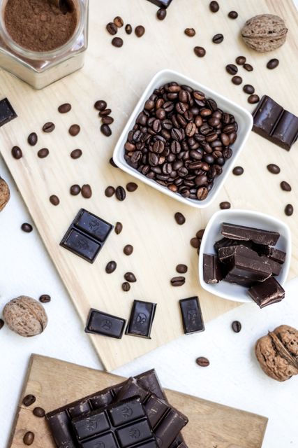 Coffee beans and dark chocolate pieces scattered on a light wooden board with whole nuts. Perfect for use in themes related to coffee, confectionery, healthy snacks, and rustic décor. Ideal for menus, recipe books, blogs, social media posts, and advertisements.