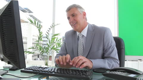 Senior Businessman Laughing at Desk During Phone Call