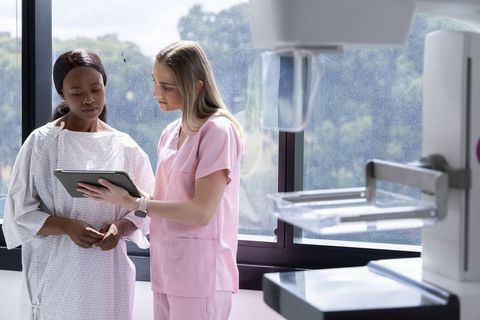 Nurse consulting female patient using tablet beside mammography machine in clinic