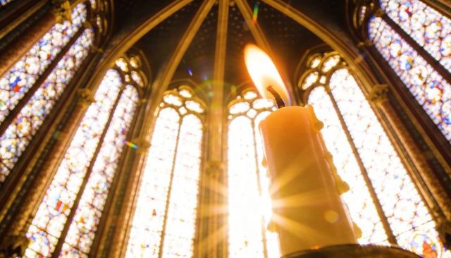 Burning candle with sunbeam in gothic chapel stained glass tracery and warm flame