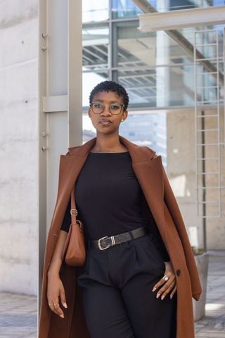 Stylish african professional woman standing in urban plaza wearing brown coat and glasses