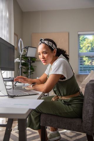 Focused young woman working remotely on laptop at home office