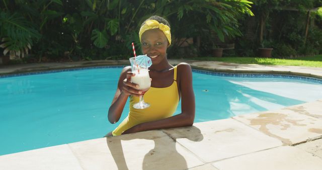 Portrait of happy african american woman standing in swimming pool making a toast with her drink. staying at home in isolation during quarantine lockdown.