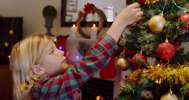 Caucasian boy decorates a Christmas tree at home. He's immersed in the festive spirit, carefully placing ornaments.