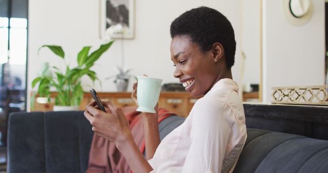 Smiling woman relaxing at home, using smartphone, holding coffee - Download Free Stock Images Pikwizard.com