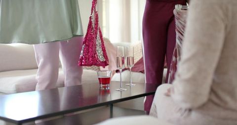 Women inspecting sequin dress and accessories at home with champagne on coffee table