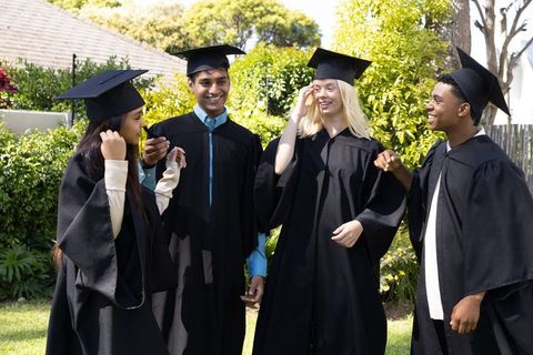 Diverse group of graduates celebrating outdoors in announcements and smiles