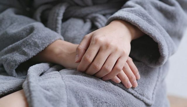 Gently interlacing hands resting on lap in gray plush bathrobe conveying calm serene soft wellness