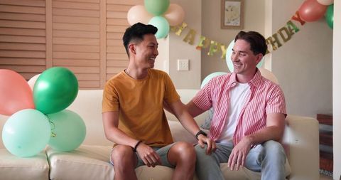 Happy Gay Couple Celebrating Birthday with Cake and Balloons Indoors