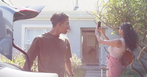 Young african american couple photographing new home on sunny front yard before trip