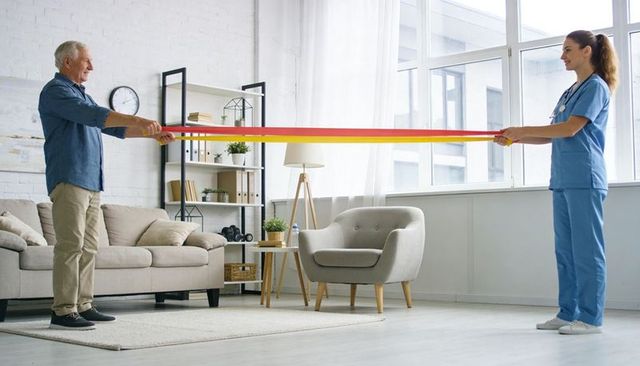 Senior man exercising with physical therapist using resistance band in bright living room
