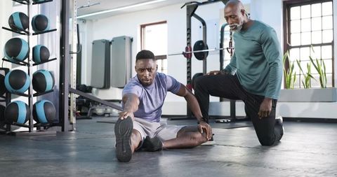 Trainer guiding athlete in flexibility stretch at modern gym