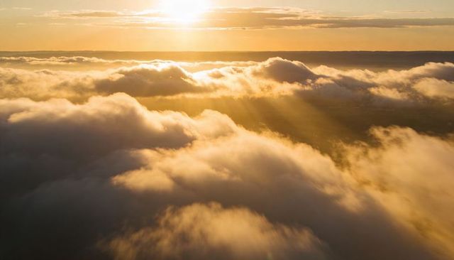 Golden sunrise streaming through thick cloud deck with sunbeams over distant horizon