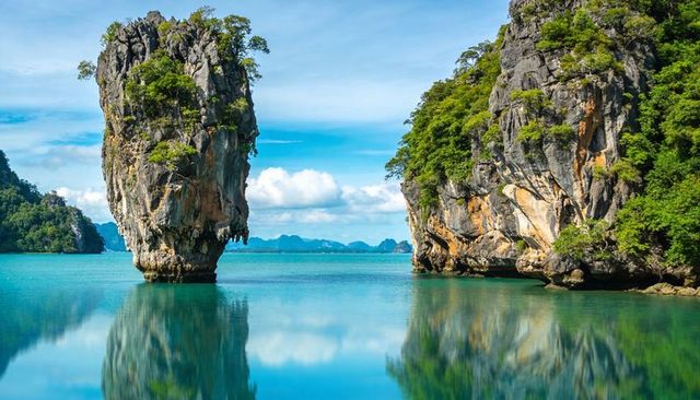 Towering limestone karst pillar reflecting on turquoise tropical bay with rugged cliff