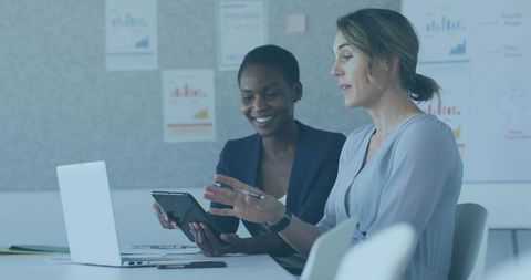 Two Professional Women Collaborating over Tablet and Laptop in Modern Office Meeting