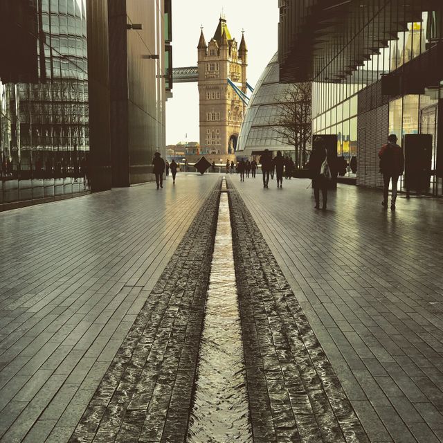 This image shows a symmetrical urban street leading to the iconic Tower Bridge in London. The moody sky and modern buildings on either side create a visually stunning contrast. Ideal for advertisements or articles related to travel, architecture, urban lifestyle, and city landmarks.