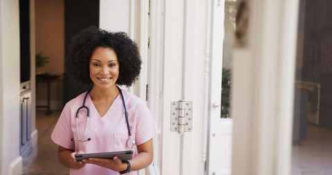 Smiling Nurse in Pink Scrubs Using Tablet in Hospital Corridor