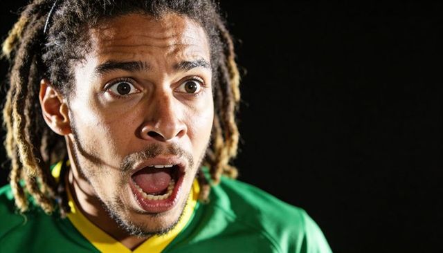 Shouting football fan with dreadlocks wearing green and yellow jersey showing shock