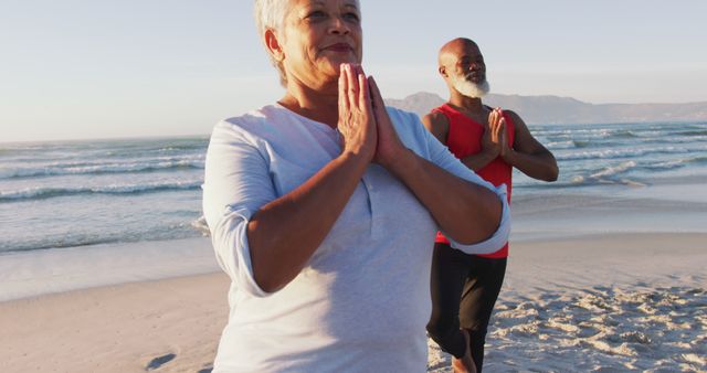 Senior couple practicing yoga on beach during sunrise. Graciously posing while meditating. Ideal for promoting wellness, fitness routines, peaceful lifestyles, and activities for the elderly. Can be used for advertising health and leisure-related services or products.