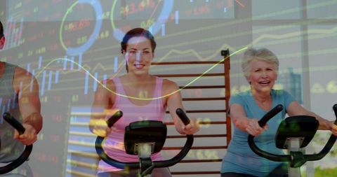 Pedaling mixed-age women in indoor cycling class with financial chart overlay for wellness