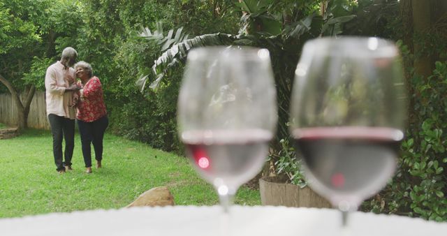 Senior biracial couple enjoys a romantic moment outdoors, with copy space. Two glasses of red wine in the foreground set the scene for a relaxing date.