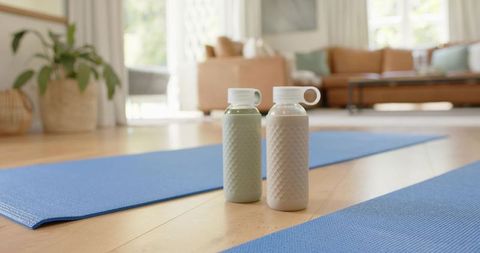 Textured reusable bottles beside blue yoga mats on hardwood floor in sunlit room