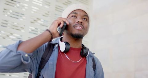 Stylish african american commuter talking on smartphone with headphones and backpack, urban