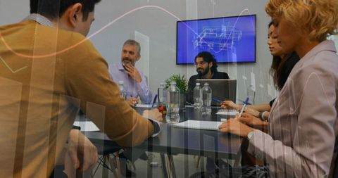 Diverse team collaborating in modern boardroom taking notes reviewing data and blueprints