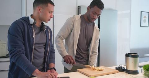 Diverse male friends chopping bananas and preparing smoothie at kitchen island