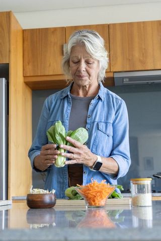 Senior woman preparing bok choy on kitchen island wearing smartwatch, healthy home cooking