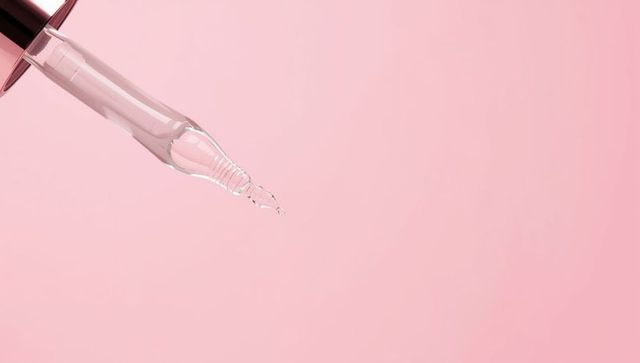 Elegant glass pipette droplet on pink background for skincare concepts