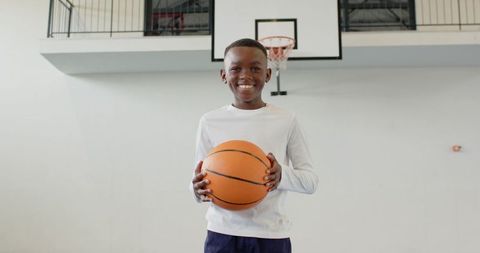 Young Boy Smiling with Basketball Indoors, Stadium Backdrop