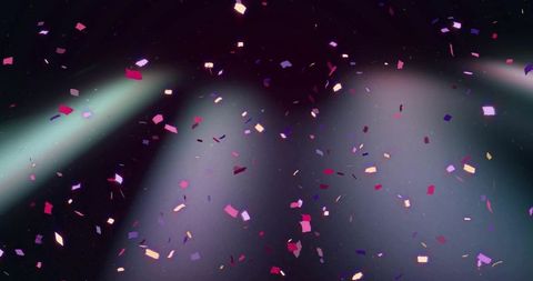 Colorful confetti falling on stage with spotlights and hazy glitter particles for events