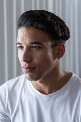 African american man in white t-shirt with double ear piercings posing by blinds headshot