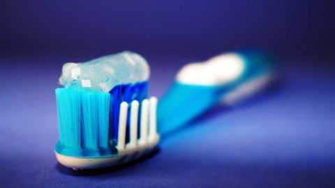 Close-Up View of Toothbrush with Blue Toothpaste on Blue Background